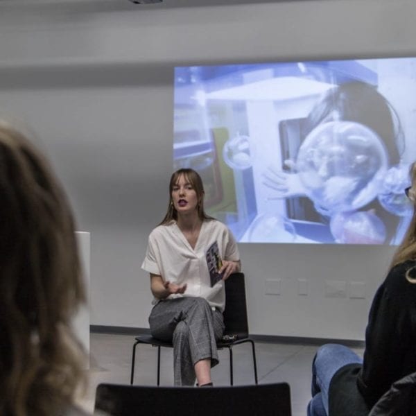 Curator Courtney Lynne Carter sits in front of a crowd talking about the videos on display