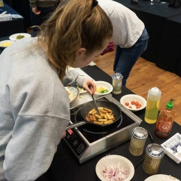 Photographed from behind, a student stirfries some spicy tofu