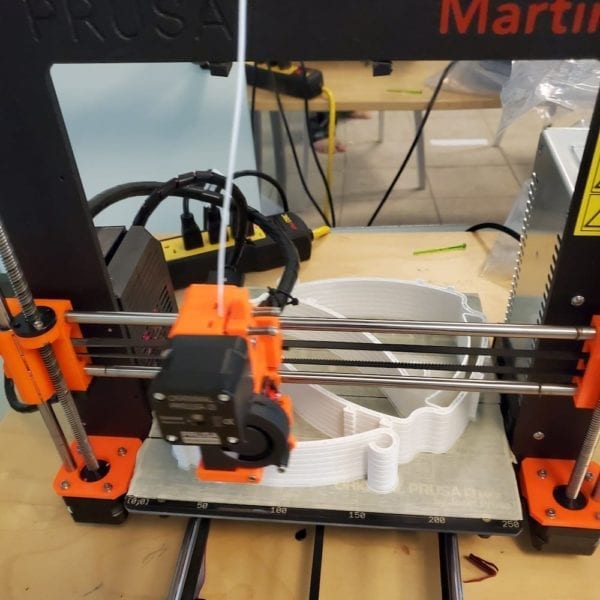 A 3D printer making white headbands for face shields.