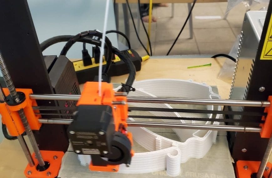 A 3D printer making white headbands for face shields.