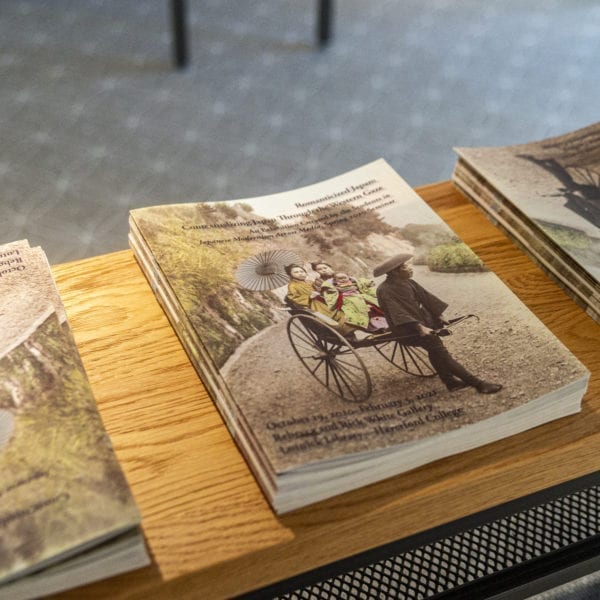 Stacks of catalogs for the "Romanticizing Japan" exhibit on a bench in the gallery.