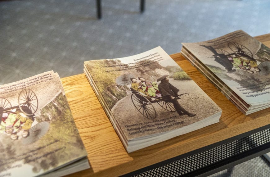 Stacks of catalogs for the "Romanticizing Japan" exhibit on a bench in the gallery.