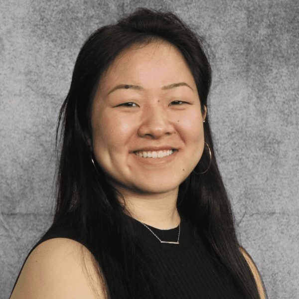Elizabeth, wearing a black dress, smiles in front of a grey background.