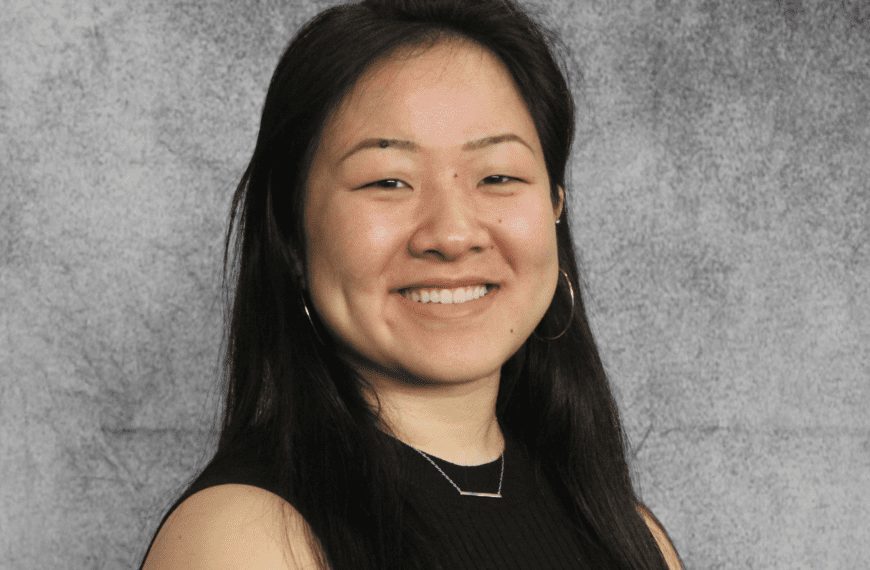 Elizabeth, wearing a black dress, smiles in front of a grey background.
