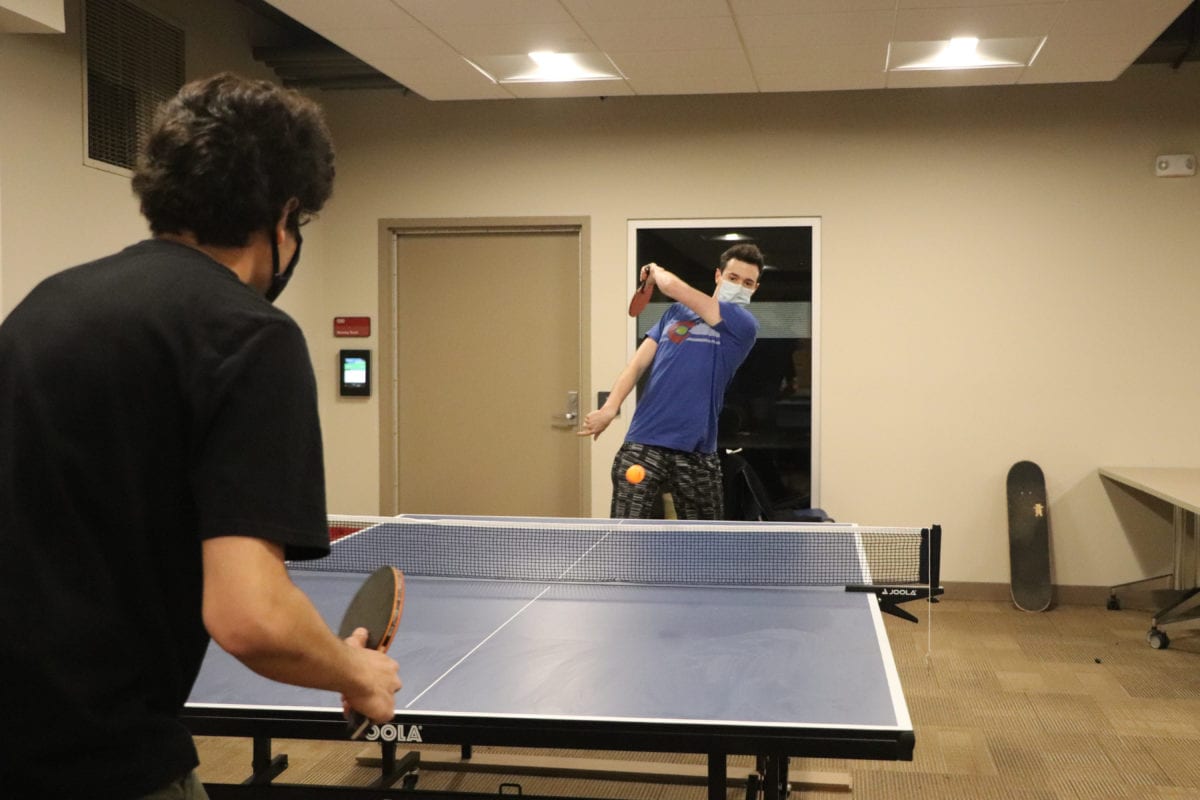 A student his a ping pong ball to another student, who crouches ready to hit it back.