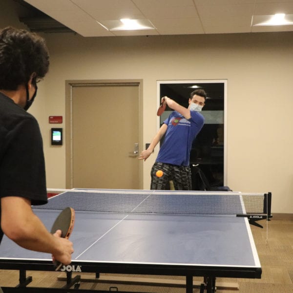 A student his a ping pong ball to another student, who crouches ready to hit it back.