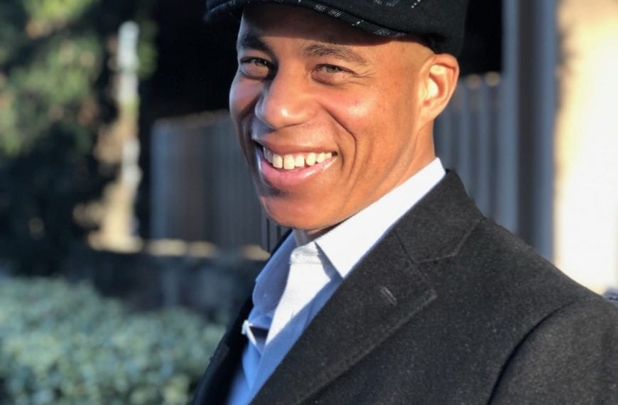 Kevin Jones wears a cap and blazer, smiling in the sunshine