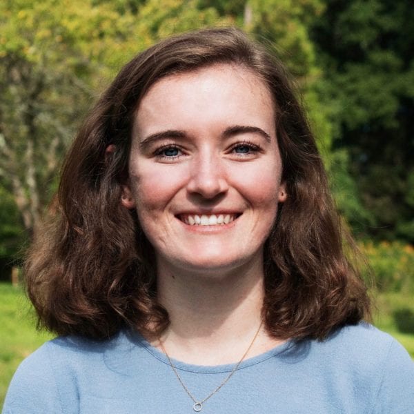 Annie Connolly-Sporing '20, wearing a blue shirt, stands in front of a background of trees.