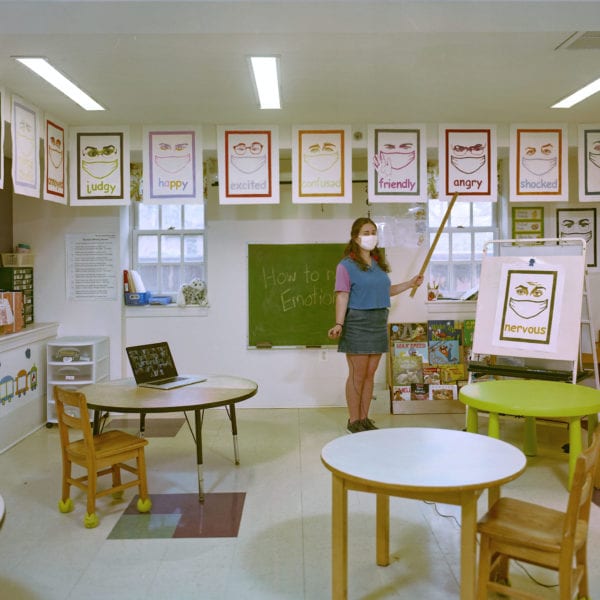 Rachel Grand BMC '21 stands in a classroom in the Phebe Thorne Anna School, showcasing some prints depicting various emotions.