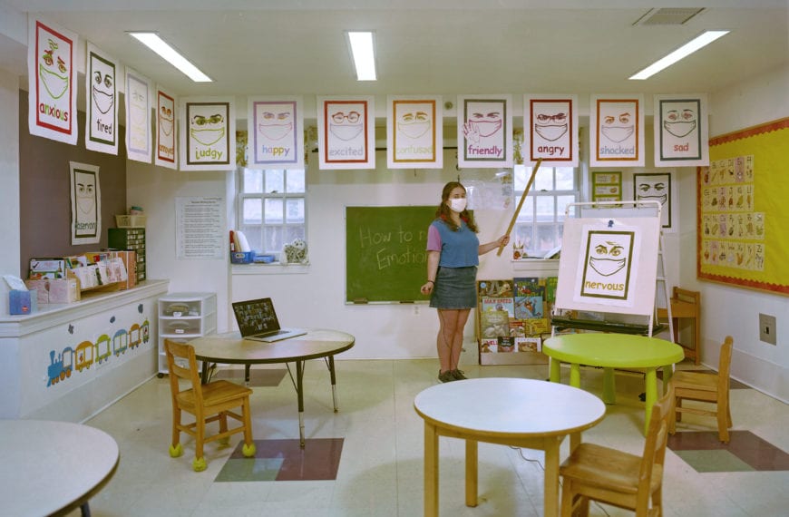 Rachel Grand BMC '21 stands in a classroom in the Phebe Thorne Anna School, showcasing some prints depicting various emotions.