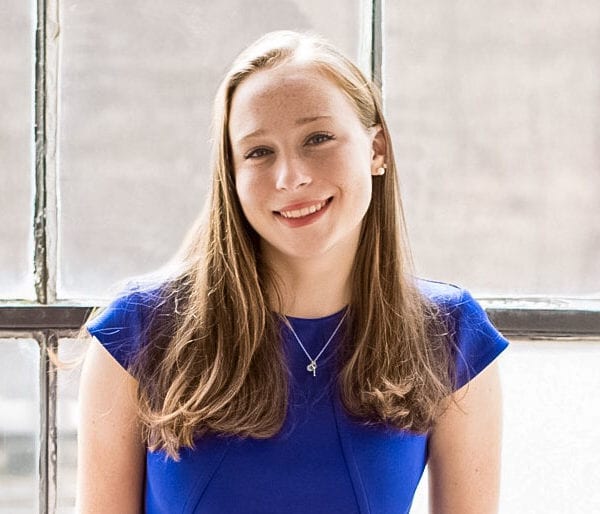 Headshot of Sarah wearing a bright blue shirt in front of a window.