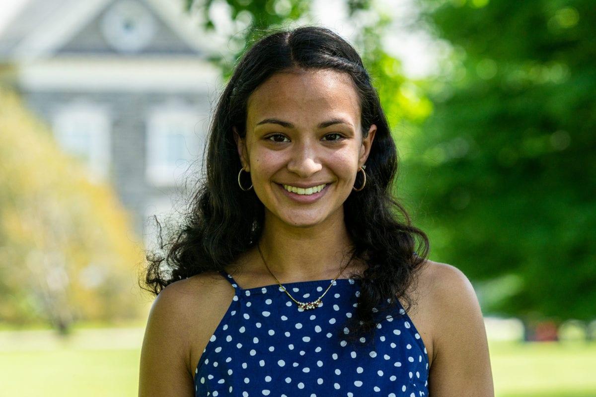 Headshot of Leela wearing a blue shirt with one polka dots with Hilles in the background