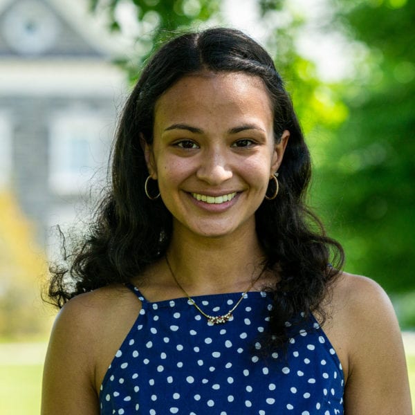 Headshot of Leela wearing a blue shirt with one polka dots with Hilles in the background