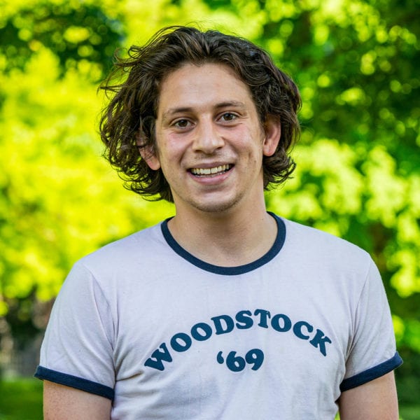 Headshot of Federico wearing white shirt with "Woodstock '69" in blue writing on it.
