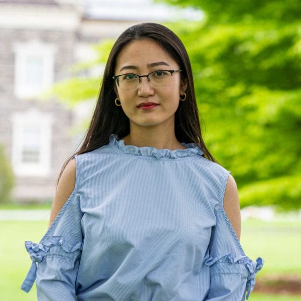 Headshot of Silvia wearing a blue blouse and standing in front of the KINSC.