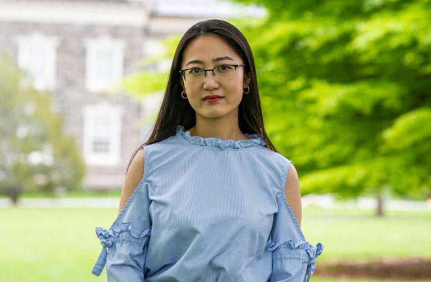 Headshot of Silvia wearing a blue blouse and standing in front of the KINSC.