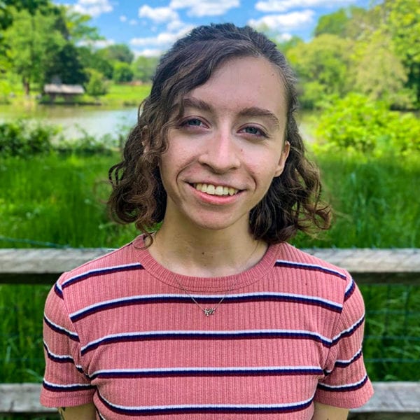 Headshot of Grace wearing a striped pink shirt in front of the duck pond.
