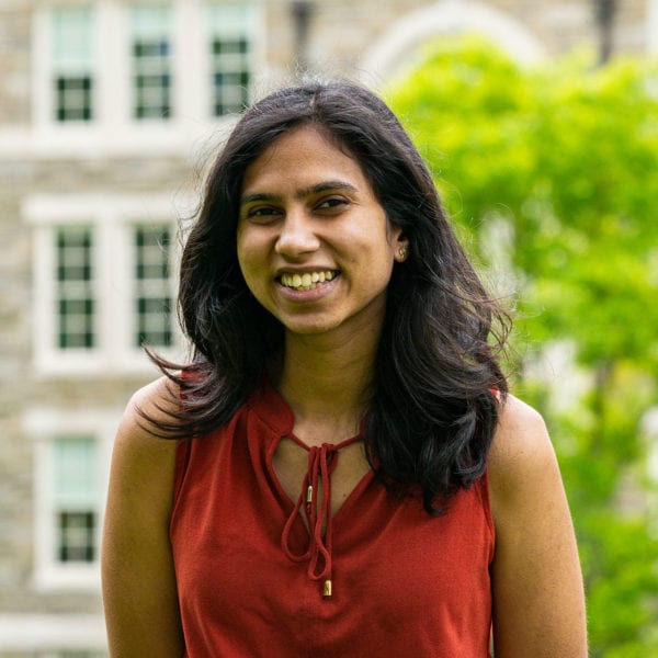 Headshot of Shreya in a red shirt standing in front of the KINSC.