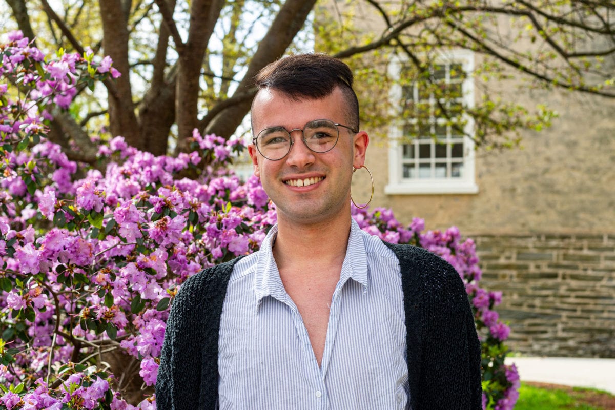 Headshot of Robbie wearing a striped shirt in front of a pink-purple bush on the side of Founders Hall.