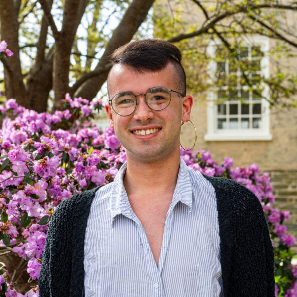 Headshot of Robbie wearing a striped shirt in front of a pink-purple bush on the side of Founders Hall.