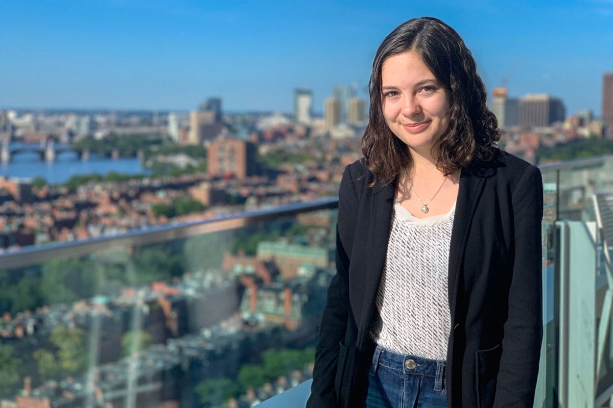 Headshot of Hannah in a patterned white shirt and suit jacket. In the background is a skyline.
