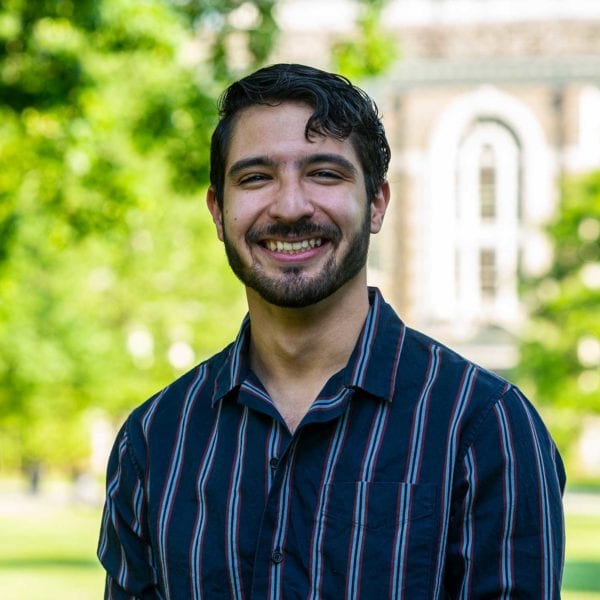 Headshot of Jan in a striped shirt with the KINSC in the background.