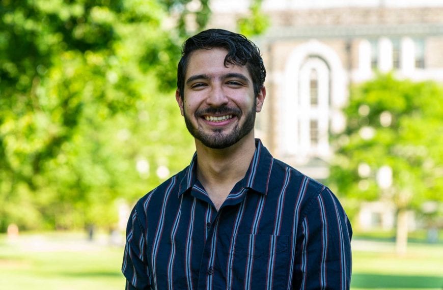 Headshot of Jan in a striped shirt with the KINSC in the background.