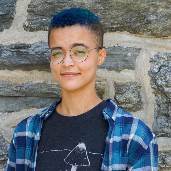 Headshot of Corinne Williams, dressed in blue, standing in front of a brick wall