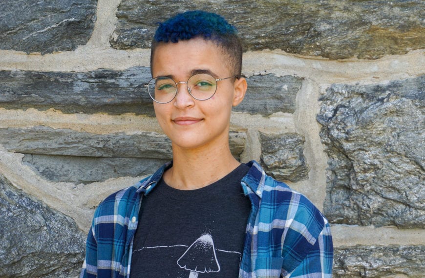 Headshot of Corinne Williams, dressed in blue, standing in front of a brick wall