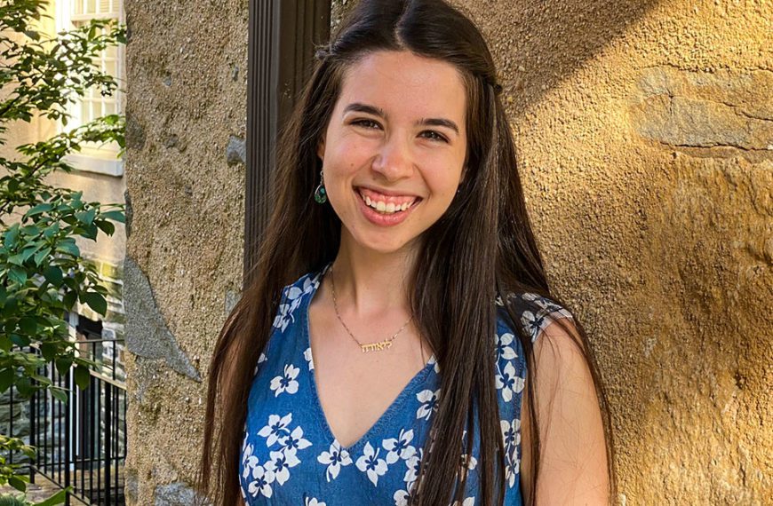 Laurel Benjamin smiles wearing a blue and white dress in Founders Courtyard