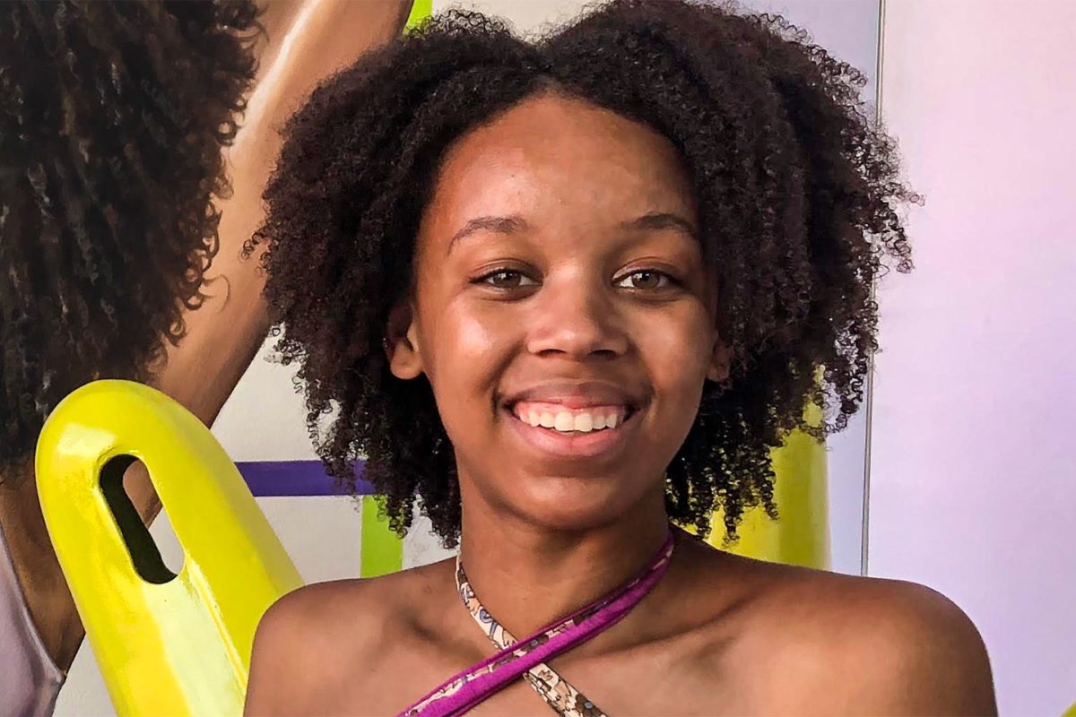 A headshot of Lourdes in a purple tank in front of a colorful painting.