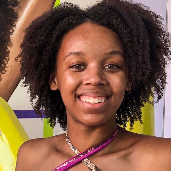 A headshot of Lourdes in a purple tank in front of a colorful painting.