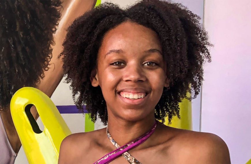 A headshot of Lourdes in a purple tank in front of a colorful painting.