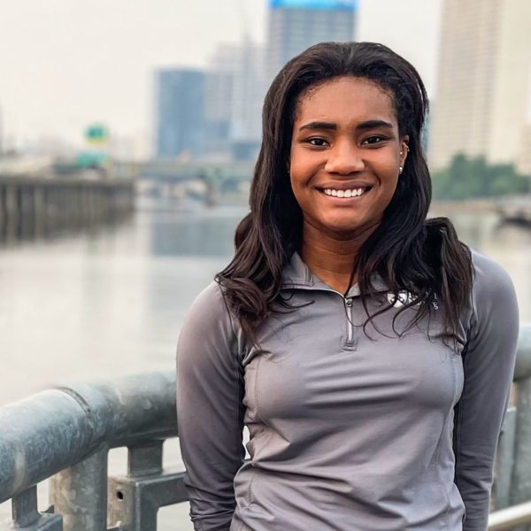 Marly stands on a bridge with a river and city skyline behind her.