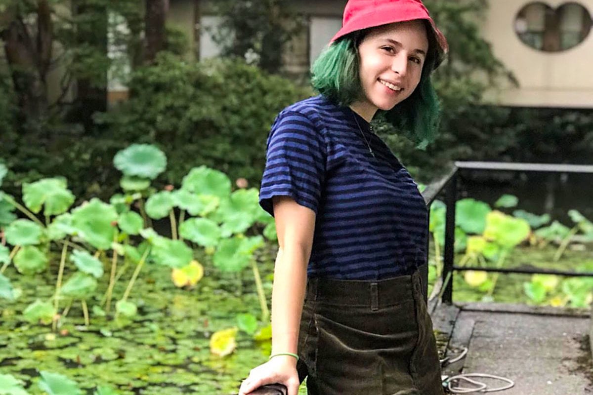 Sophie wearing a casual outfit smiling on a platform looking over a lilypad covered pond.