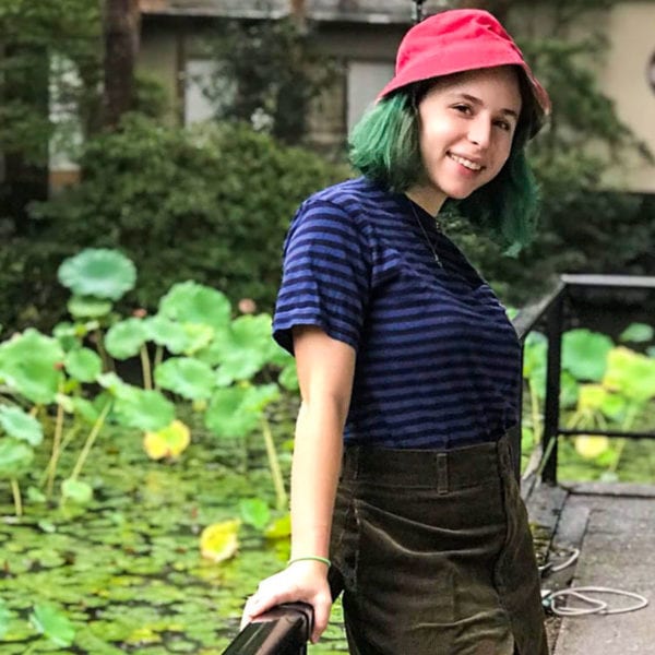 Sophie wearing a casual outfit smiling on a platform looking over a lilypad covered pond.