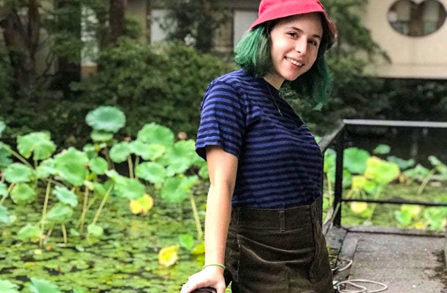 Sophie wearing a casual outfit smiling on a platform looking over a lilypad covered pond.