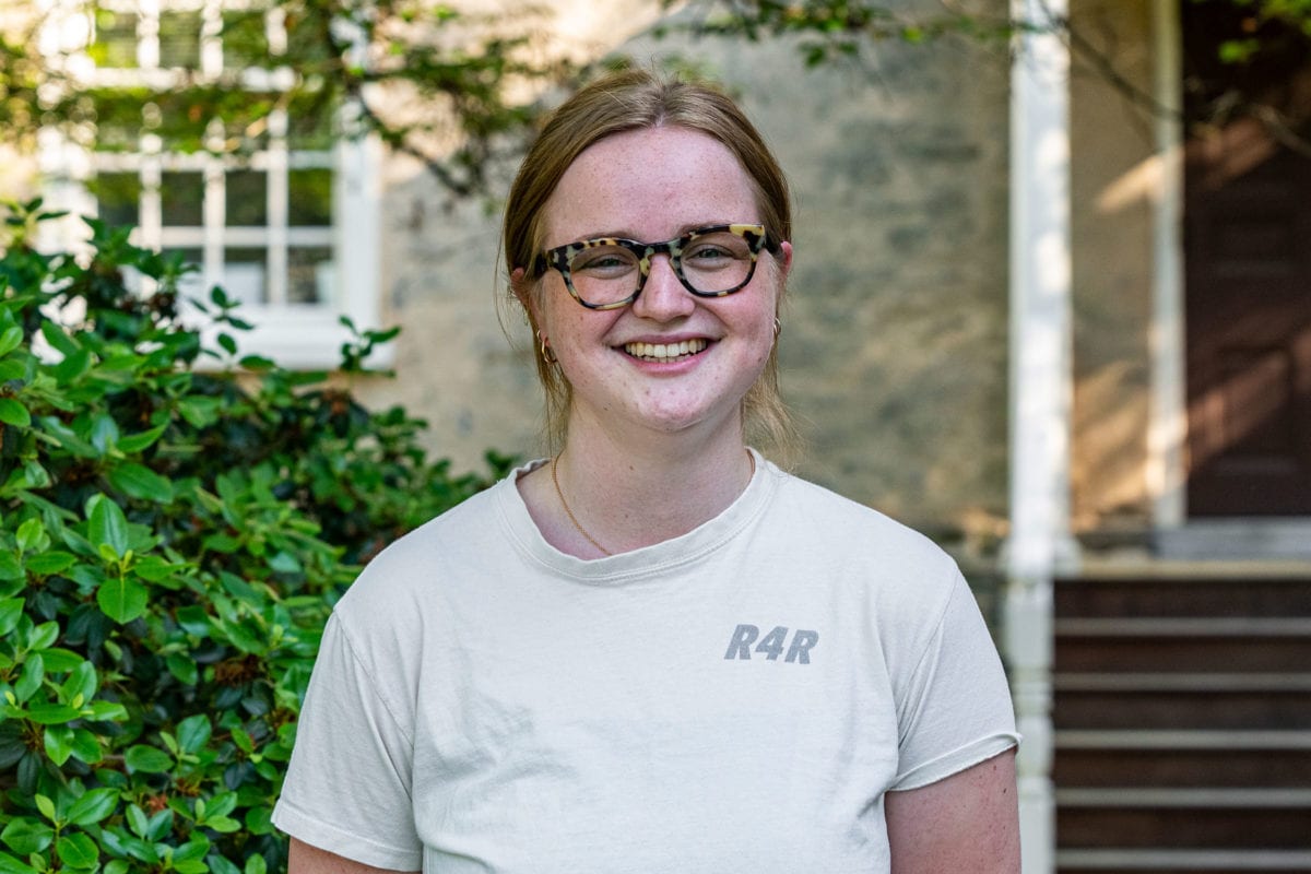 A headshot of Fiona wearing a white short-sleeved shirt standing in front of Founders Hall.