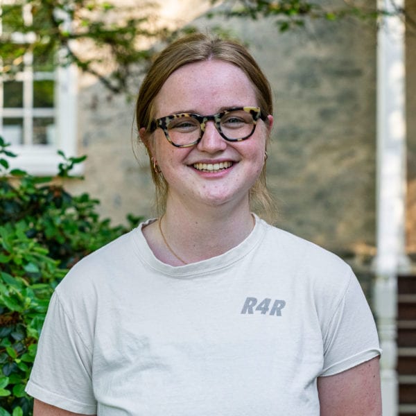 A headshot of Fiona wearing a white short-sleeved shirt standing in front of Founders Hall.
