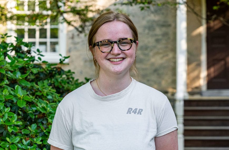 A headshot of Fiona wearing a white short-sleeved shirt standing in front of Founders Hall.