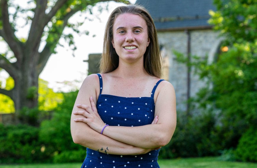 A picture of Molly in a blue dress with white polka dots, standing in front of the library.