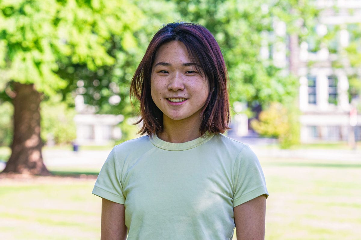 Headshot of Shufan in a yellow-green shirt standing in front of the KINSC.
