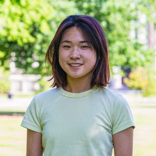 Headshot of Shufan in a yellow-green shirt standing in front of the KINSC.
