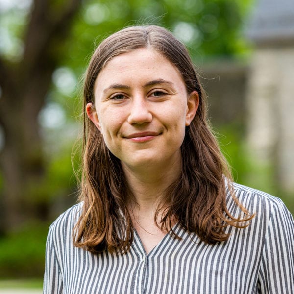 A headshot of Charlotte in front of Magill, wearing a striped button-down.