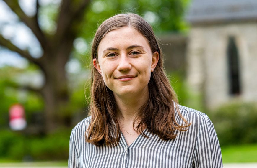A headshot of Charlotte in front of Magill, wearing a striped button-down.