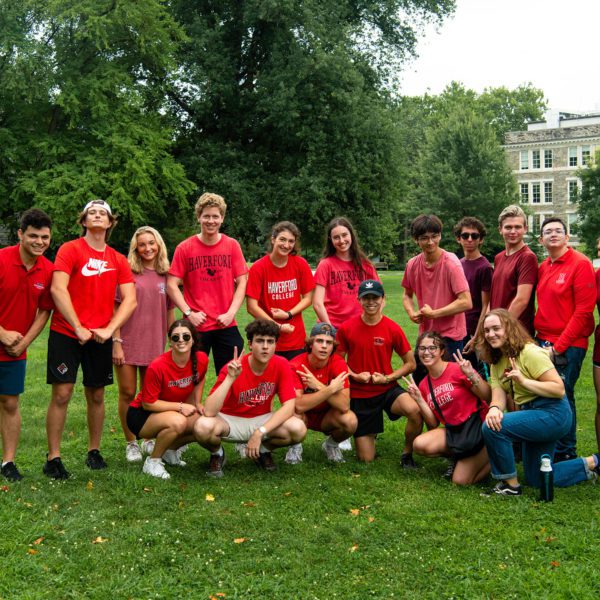 A group of students in red t-shirts, many reading "Haverford" across the front, pose on Founders Green.