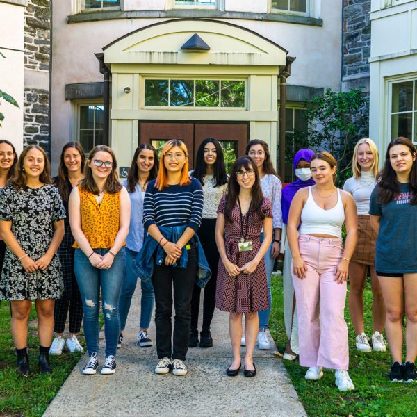 Fourteen students stand in front of the entrance to the KINSC Rotunda.