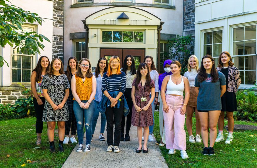 Fourteen students stand in front of the entrance to the KINSC Rotunda.