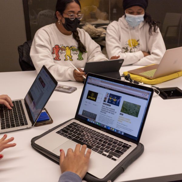 An open laptop displays Jolt Magazine with two masked students visible behind it.