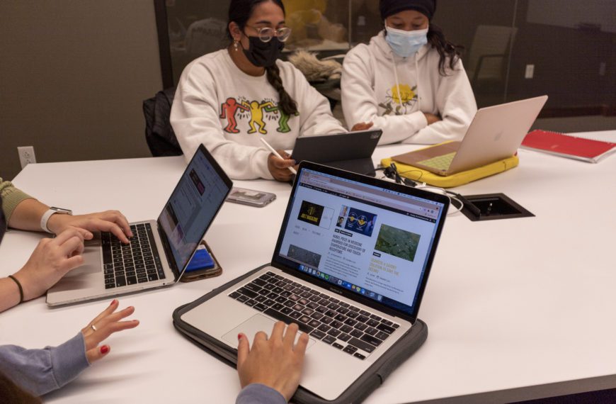 An open laptop displays Jolt Magazine with two masked students visible behind it.